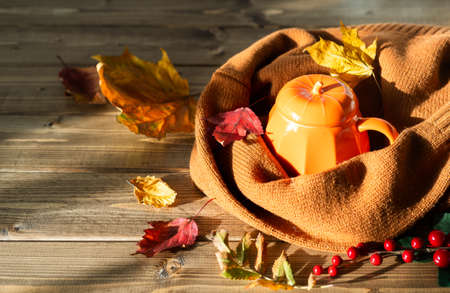 Composition with orange pumpkin styled cup of coffee and autumn themed decoration, fallen leaves, cozy sweater on brown wooden background. copy space.の写真素材