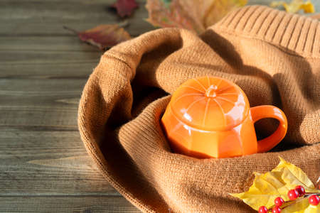 Composition with orange pumpkin styled cup of coffee and autumn themed decoration, fallen leaves, cozy sweater on brown wooden background. copy space.の写真素材