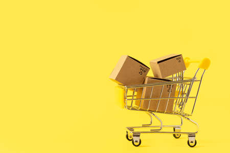 Toy shopping cart with boxes in female hand over blue background. Copy space for text or design. Ssale, discount, shopaholism concept. Consumer society trend.の写真素材