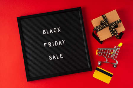 Text Black friday on black letter board, gift, shopping cart and credit card and on red background. Concept season sales time. Flat lay Top view Copy space Template layout for your design.の写真素材