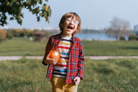 Cute boy in glasses play with shine light pumpkin in autumn park on Halloween. Kids trick or treat....