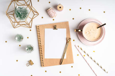 Desktop blank planner. Flat lay of white working table background with cup of coffee and Christmas decoration. Top view balls, fir tree, paper clips, mock up greeting card, craft Notebook and pen.の写真素材