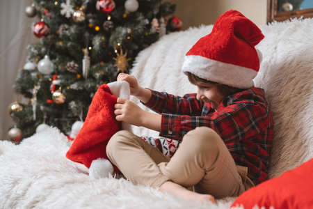 Cute little boy in red hat waiting Santa Claus in living room with Christmas tree at homeの写真素材
