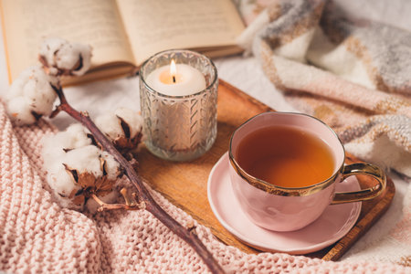 Details of still life in the home interior of living room. Sweater, cup of tea, cotton, cozy, book, candle. Moody. Cosy autumn winter concept. Decoration, vintage with glow bokeh.の写真素材