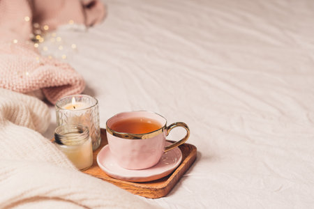 Details of still life in the home interior of living room. Sweater, cup of tea, cotton, cozy, book, candle. Moody. Cosy autumn winter concept. Decoration, vintage with glow bokeh.の写真素材