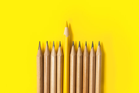 One yellow pencil standing out from the series of gray pencils. On yellow background. Sign symbol idea concept of leadership, divergent, diversity. Standoff of the individual to societyの写真素材