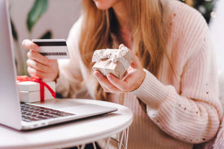 Close up of woman hands with credit card, gifts and laptop. Online shopping at Christmas, valentine day or birthday holidays. Freelance girl woking from home officeの写真素材