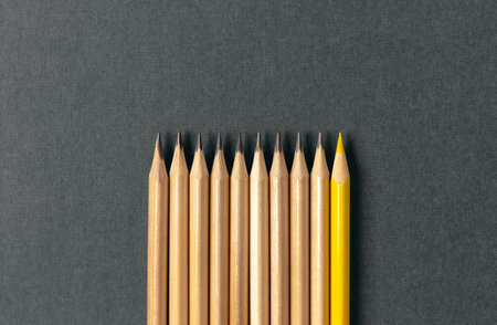 One yellow pencil standing out from the series of gray pencils. On grey background. Sign symbol idea concept of leadership, divergent, diversity. Standoff of the individual to society.の写真素材