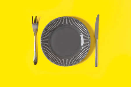 Flat lay with mock up gray plate and cutlery on trendy yellow background with copy space....