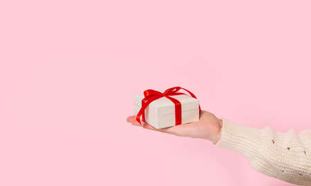 Beauty Woman hands holding Gift box with red bow on pink background, close-up. pastel colors, copy space for text. Valentine gift. Banner for Christmas, hew year, birthday concept.の写真素材