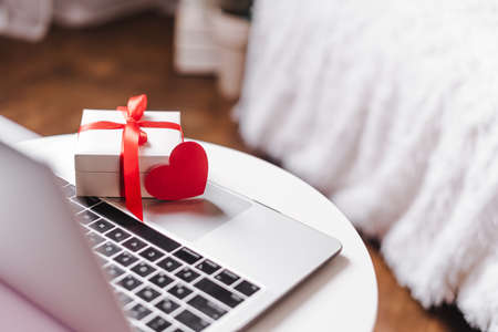 White Gift box or presents with red heart on laptop, online shopping concept. Valentine greeting card with copy space. Christmas, birthday or Valentine day holidaysの写真素材