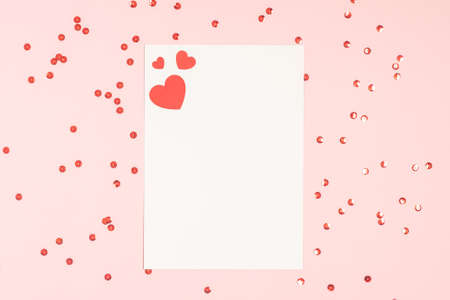 Top view of blank mock up paper greeting or invitation card over pink pastel background with red...