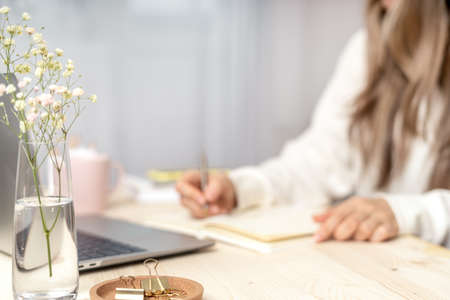 Distance learning online education and work. Business woman writes goals, plans, make to do and wish list in notebook on desk, working from home office. Using laptop.の写真素材