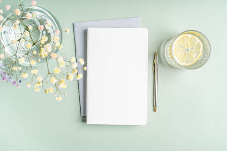 Top view blank paper Notebook, flowers, water with lemon and pen. Desktop mock up, Flat lay of green working table background with office equipment, mockup greeting cardの写真素材