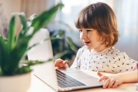 Distance learning online education. Caucasian smile kid boy studying at home with laptop and doing school homework. Thinking child siting at table with notebook. Back to school.の写真素材