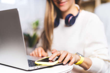 Freelance woman with headphones and laptop texting at mobile cell phone and online shopping, sitting...