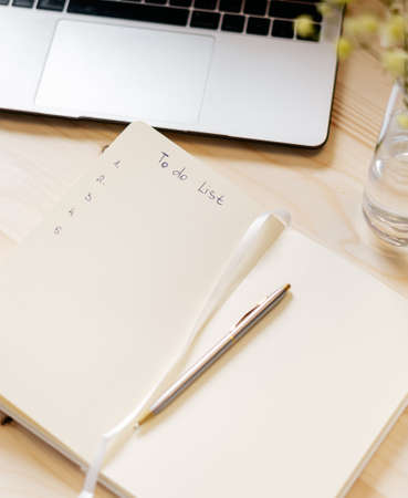 Top view blank paper Notebook with to do list, flowers, laptop keyboard, cup of coffee and pen....