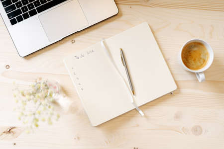 Top view blank paper Notebook with to do list, flowers, laptop keyboard, cup of coffee and pen. Desktop mock up, Flat lay of wooden working table background with office equipment, mockup.の写真素材