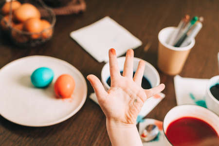 Easter day. Dirty hand of Kid boy painting eggs on wooden background. Child sitting in a kitchen. Preparing for Easter, creative homemade decoration.の写真素材
