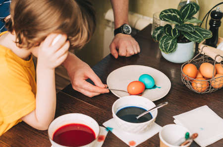 Easter day. Father and son painting eggs on wooden background. Family sitting in a kitchen. Preparing for Easter, creative homemade decoration.の写真素材