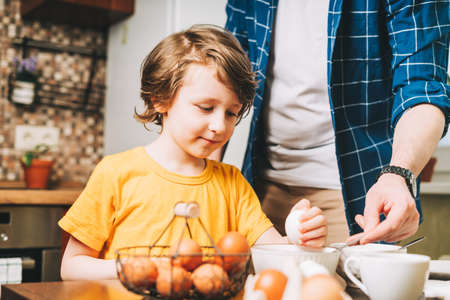 Easter day. Father and son painting eggs on wooden background. Family sitting in a kitchen. Preparing for Easter, creative homemade decoration.の写真素材