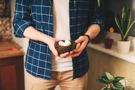 Easter day. Adult man holding basket with eggs on wooden background. Stay in a kitchen with nest. Preparing for Easter, creative homemade decoration.の写真素材