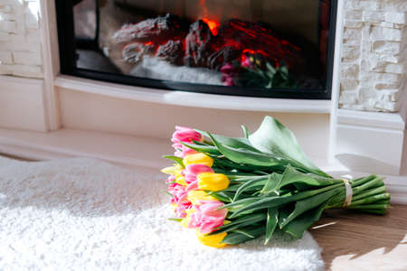 Fresh spring yellow and pink tulips bouquet on the fur carpet floor by the fireplace with copy space for text. Love, easter, International Women, Mother and Happy Valentine day conceptの写真素材