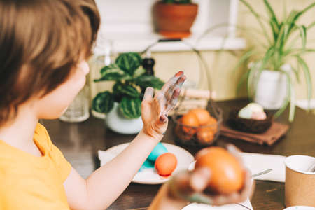 Easter day. Cropped close up Kid boy with dirty hands painting eggs on wooden background. Child sitting in a kitchen. Preparing for Easter, creative homemade decoration.の写真素材