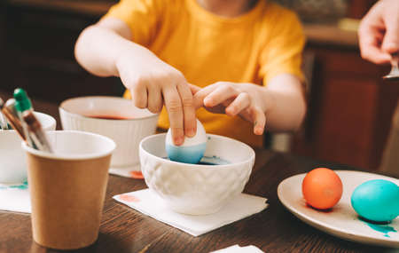 Easter day. Cropped close up Kid boy hands painting eggs on wooden background. Child sitting in a kitchen. Preparing for Easter, creative homemade decoration.の写真素材