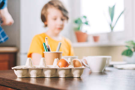 Easter day. Kid boy painting eggs on wooden background. Child sitting in a kitchen. Preparing for Easter, creative homemade decoration.の写真素材