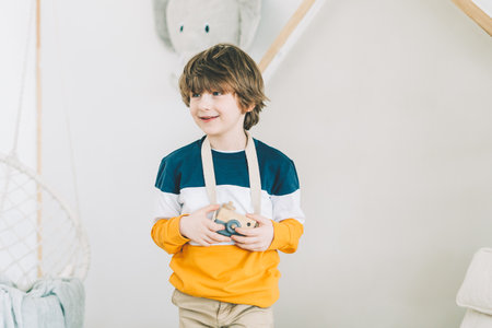 Smiling caucasian little Cute preschooler child boy having fun and playing. Kid acting like a professional photographer taking photos at home in kids room. Background with copy spaceの写真素材
