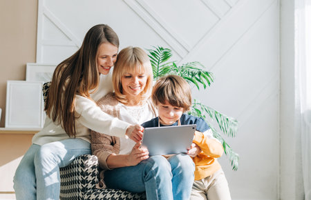 Family Mature senior woman with adult daughter and child kid boy using digital tablet computer device. Caucasian grandmother, daughter and grandson at home. Mother and son having online video chatの写真素材