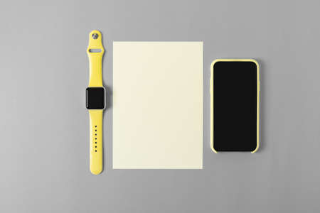 Flat lay mock up mobile cell phone, blank paper and watch on clean office desk. Illuminating Yellow...