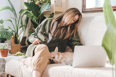 Freelance woman falling asleep with dog and tired, while working from home office at laptop...