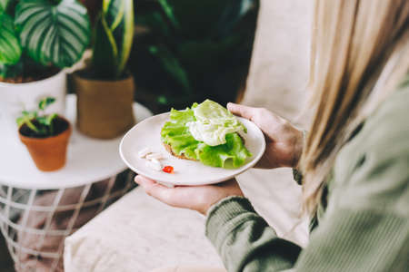 Close up of woman hands holding a plate, and choosing vegetables or tablet vitamin pills. Beautiful girl in living room with plants at home, healthy lifestyle concept.の写真素材