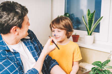 Happy Fathers day. Dad painted on the nose of child kid boy on Easter. Funny portrait of smiling caucasian father and his son painting with watercolor at homeの写真素材