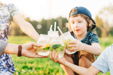 Family with two children summer picnic in nature. Little boys hold yellow and green glasses with...