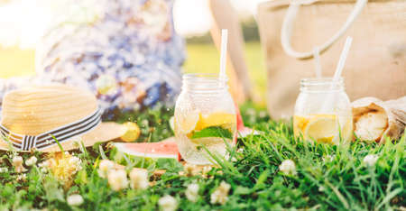 Fresh Homemade Lemonade With lime and lemon On The Grass in sunny park. Blurred green grass and people summer background. Outdoors Picnic, relaxation concept. Hello weekend.の写真素材