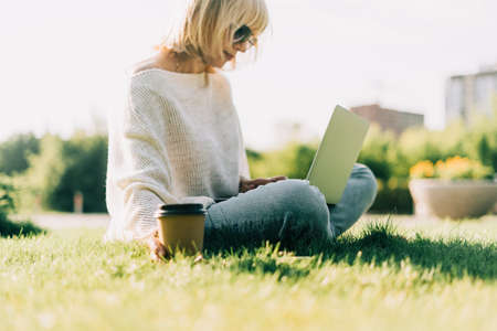 Close up coffe cup. Adult Woman typing at laptop and mobile cell phone outside in park. Thinking...