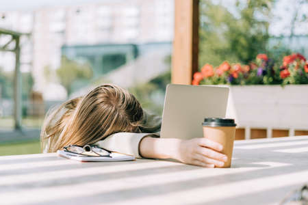Beautiful blonde business woman tired and lying on keyboard while working at laptop, sit down...