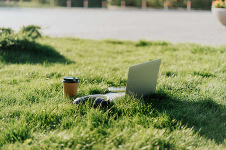 Headphones, laptop, mobile phone on the grass. Listen to music and working concept. Coffee cup and cellphone. Summer background.の写真素材