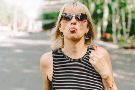 Portrait of happy mature adult woman making faces sticking her tongue out. Senior shows her tongue...