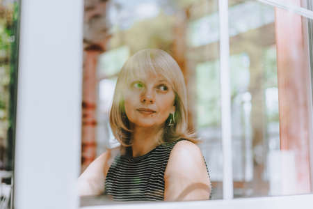 Senior woman sits in front of the window. Mature adult woman looking sad and thoughtful. Mental...