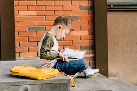 Back to school. Cute child with backpack, holding notepad and training books going to school. Boy pupil with bag. Elementary school student going to classes. Kid sitting on stairs outdoors.の写真素材