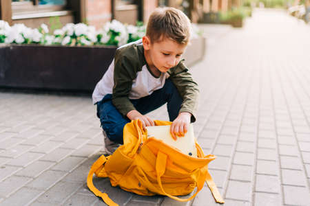 Back to school. Cute child packing backpack, holding notepad and training books going to school. Boy pupil with bag. Elementary school student going to classes. Kid walking outdoor on the city street.の写真素材