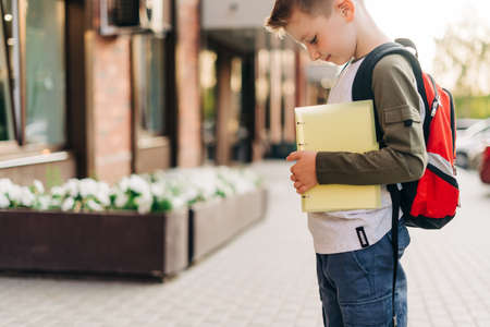 Back to school. Cute child with backpack holding notepad and training books going to school. Boy pupil with bag. Elementary school student going to classes. Kid walking outdoor on the city street.の写真素材