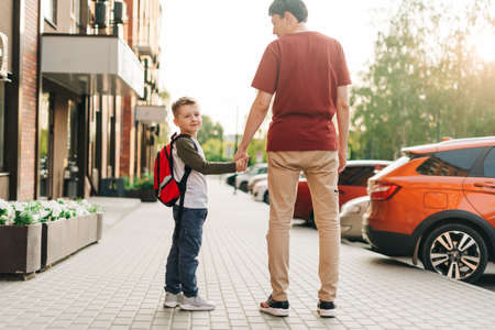 Happy father and kid son going to classes. Parent take child boy to school in first grade. Pupil of primary school go study with backpack outdoors in city street. Beginning of lessons. Back to school.の写真素材