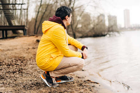 Young man sit on the shore of the lake outdoors over autumn park background. Fallen leavesの写真素材