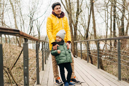 Father in yellow raincoat and son having fun in forest. Happy family with child kid boy playing and having fun outdoors over autumn park background.の写真素材