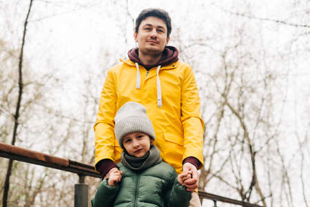 Father in yellow raincoat and son having fun in forest. Happy family with child kid boy playing and having fun outdoors over autumn park background.の写真素材